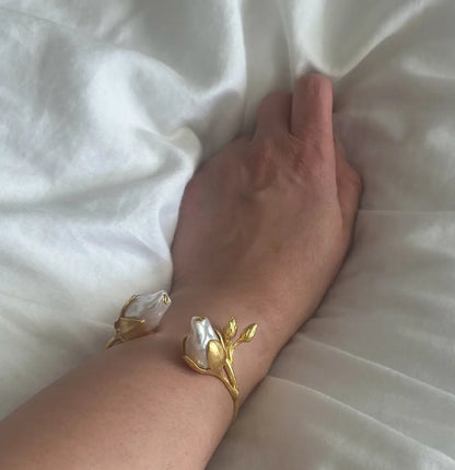 Gold cuff bracelet with floral design on a wrist against a white fabric background