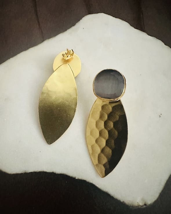 Gold-plated artisanal sustainable bold earrings with gray gemstones on a white marble slab