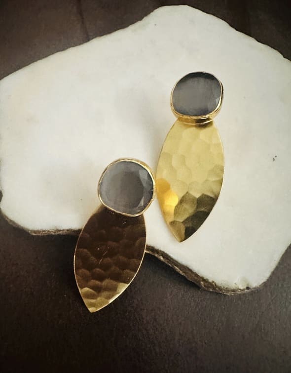 Artisanal Gold-plated bold statement earrings with gray gemstones on a white stone surface