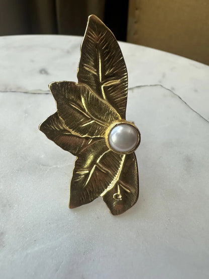 Gold-plated sustainable contemporary flower-shaped ring with a pearl center on a marble surface