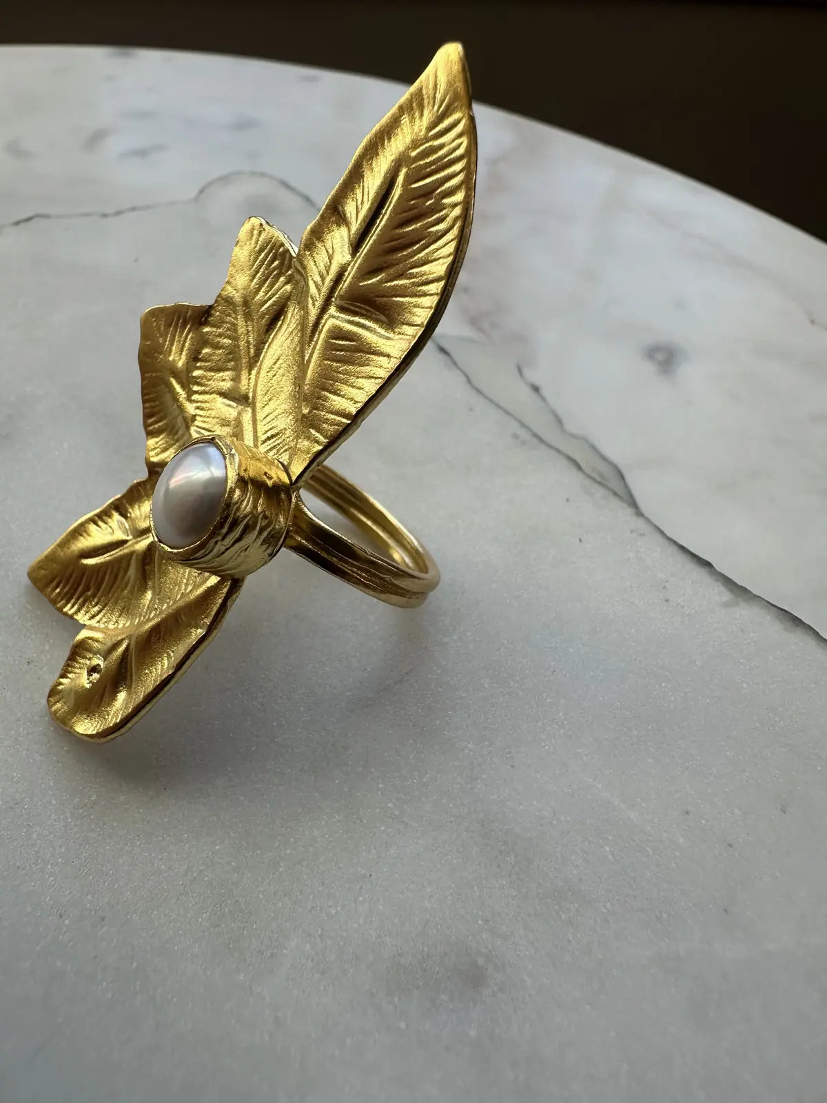 Handmade Gold flower-shaped ring with a pearl gemstone on a marble surface
