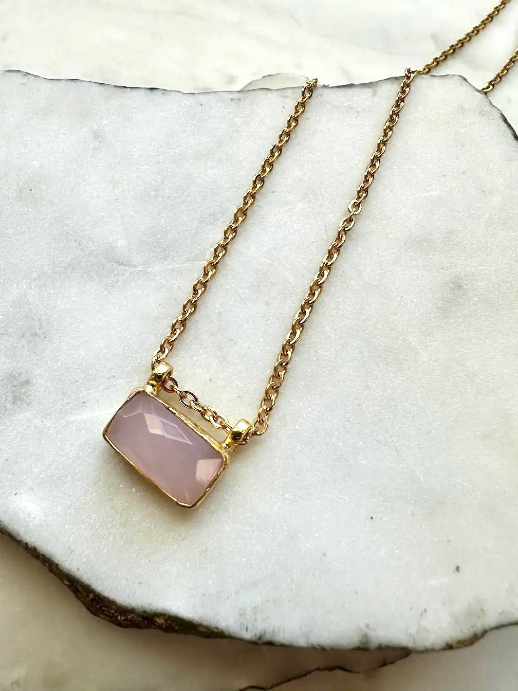 Gold plated rose quartz pendant necklace with on a marble surface