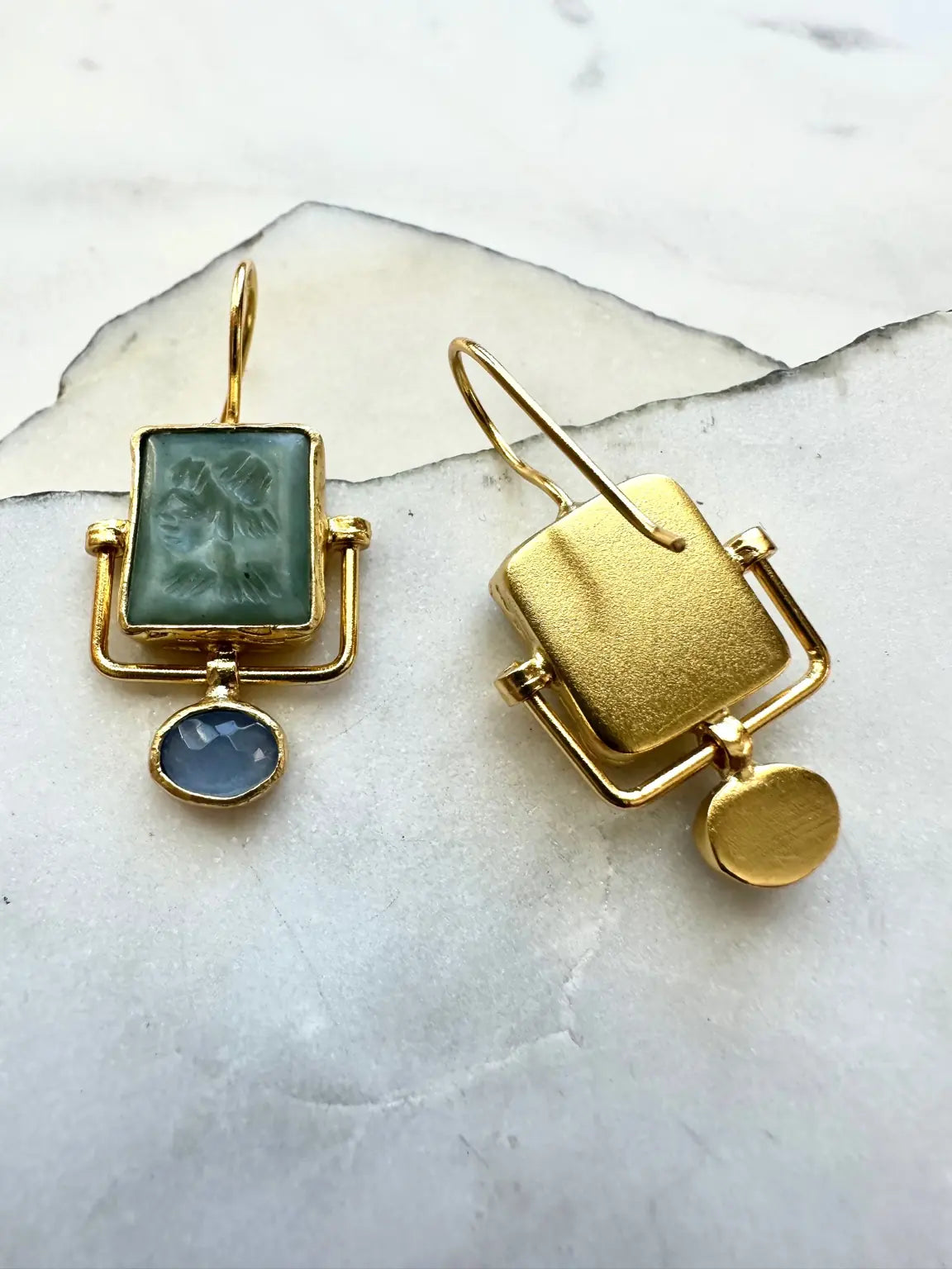 Gold plated contemporary earrings with green jade and blue chalcedony stones on a marble surface