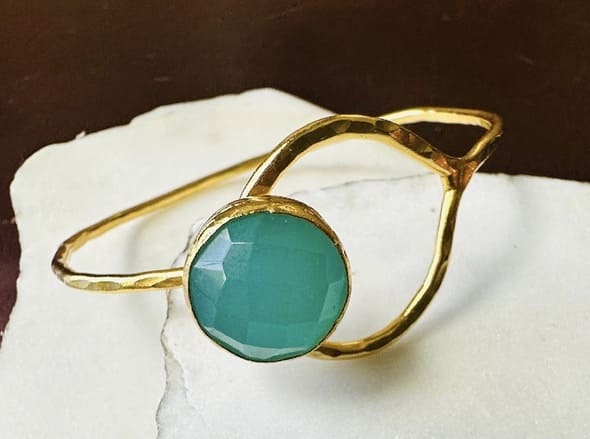 Artisanal gold-plated bracelet with round aqua chalcedony gemstone placed ok white marble backdrop