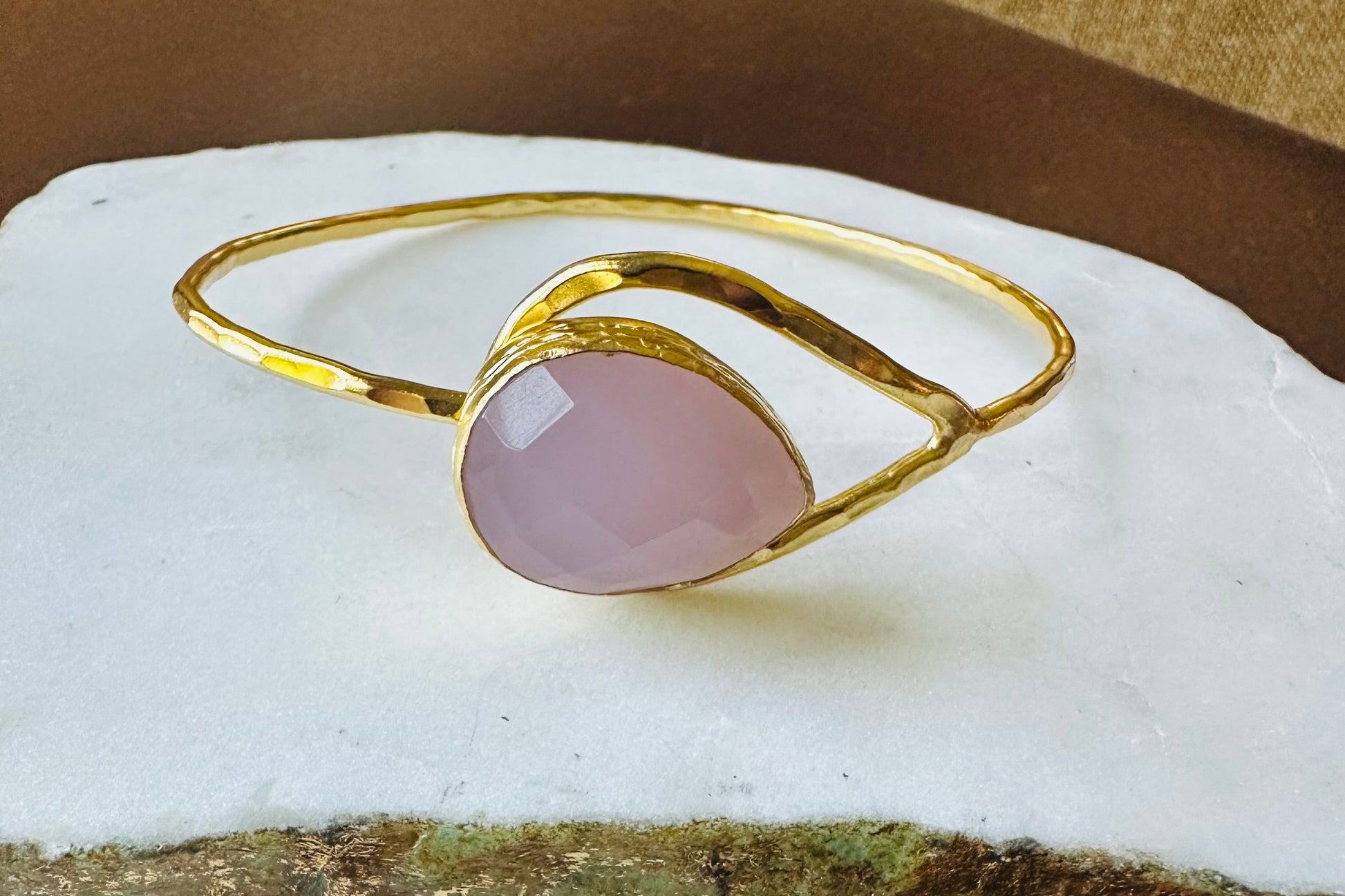 Gold bracelet with a pink stone on a white rock