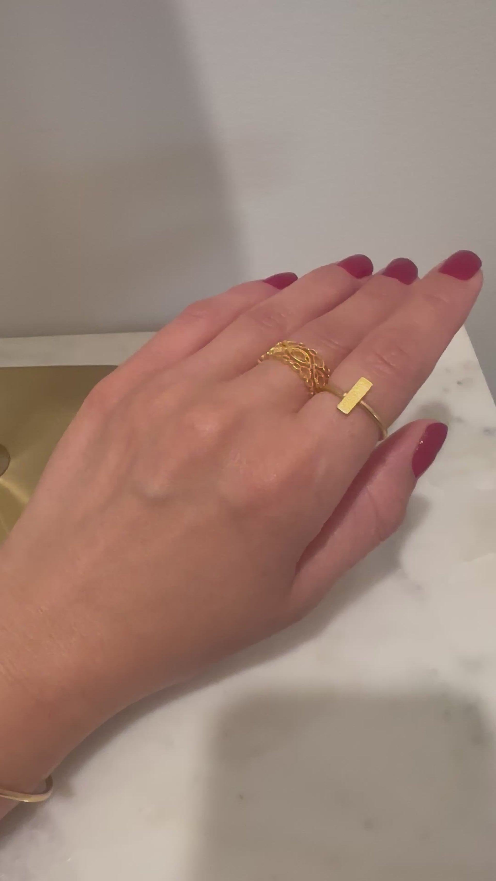 Video of a hand wearing beautiful dainty waterproof 21k gold-plated bracelet with rectangle in center and matching ring on index finger. The middle finger has a gold-plated lace designed band. The Bebek Jewels jewelry is waterproof.