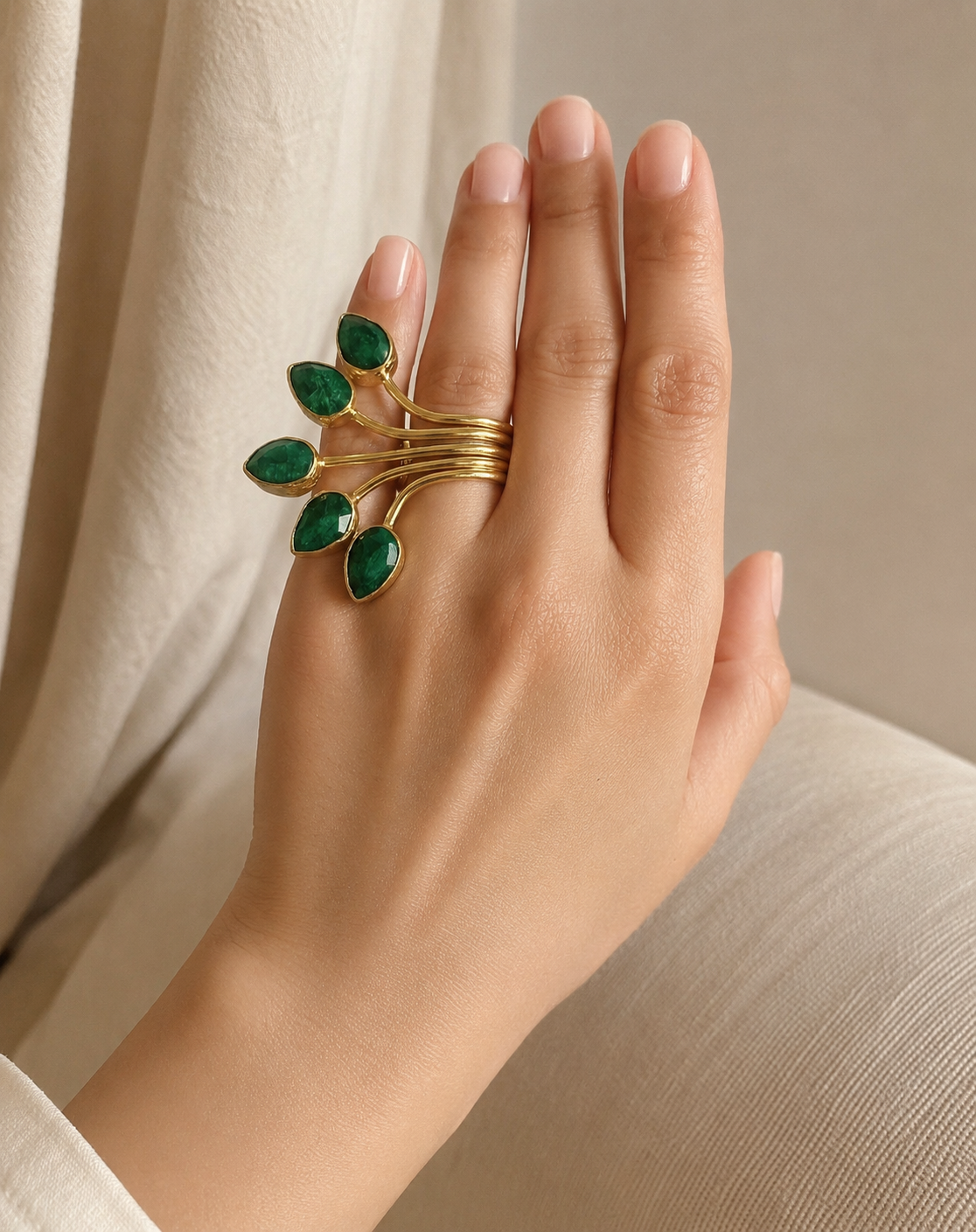 woman’s hand wearing A gold-plated fan multi-stone emerald ring with five leaf-like branches, shown against a neutral background